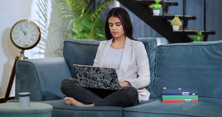 Indian Asian gen z busy young female girl sitting sofa couch do online job work from home study...