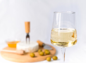 A wineglass of white wine and in the background appetizer of camembert cheese and olives. Close-up. Selective focus.