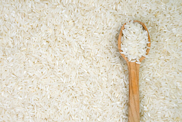 White long rice in a wooden spoon on a rice background. Banner. Top view. Close-up. Selective focus.