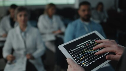 Close up shot of hands of male speaker zooming line graph on digital tablet while giving presentation to audience on medical conference