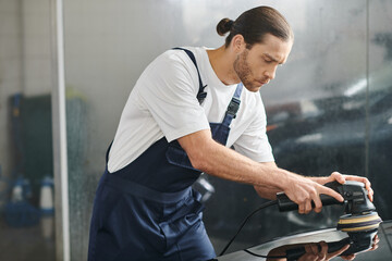 handsome hard working serviceman in uniform with collected hair using polishing machine on black car