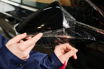 cropped view of hard working dedicated serviceman applying protective foil on mirror of black car