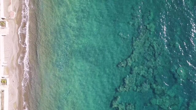Gentle Waves: Stationary Drone Video Captures Serene Beach Scene Next to Cityscape