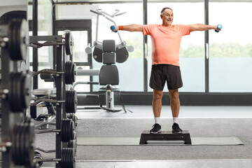 Mature man exercising step aerobic and holding dumbbells at the gym