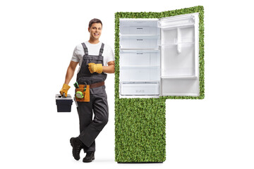 Full length portrait of a repairman with a tool box leaning on a power efficient fridge