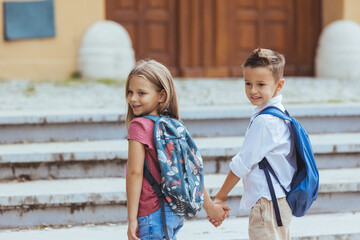 Young children walking to school. Two cute little children walking to school. Portrait of smart friends with backpacks walking down city road on sunny day