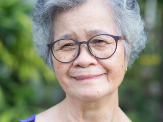 Senior Asian woman looking at the camera with a smile while standing in the garden.