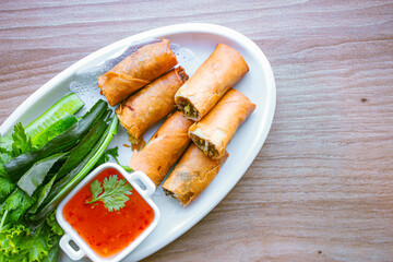 Freshly fried golden yellow spring rolls on a white plate with various vegetables and a delicious dipping sauce, top view.