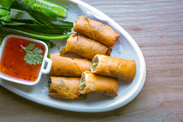Freshly fried golden yellow spring rolls on a white plate with various vegetables and a delicious...