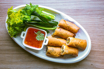 Freshly fried golden yellow spring rolls on a white plate with various vegetables and a delicious dipping sauce, top view.