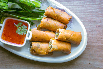 Freshly fried golden yellow spring rolls on a white plate with various vegetables and a delicious...