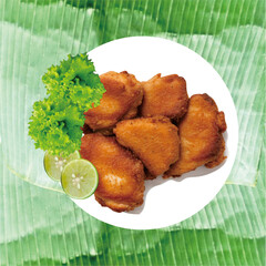 Enjoy fried chicken with spices served on a white plate covered with green banana leaves