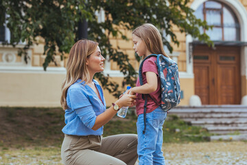Happy family preparing for school. Little girl with mother. Mother saying goodbye to her daughter at school. Beginning of lessons. First day of fall.