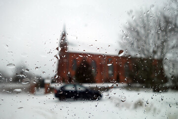 View on winter church and car through wet windshield with rain drops.