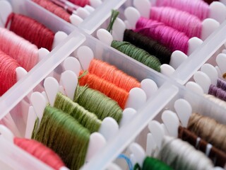 A close-up shot of a plastic sorting box full of bobbins with different colour embroidery threads.