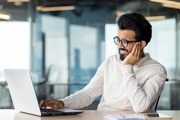Obraz premium Severe pain and inflammation in the ear bothers a young Indian man, a businessman who works in an office. He sits by the tholos and holds his hand by his ear