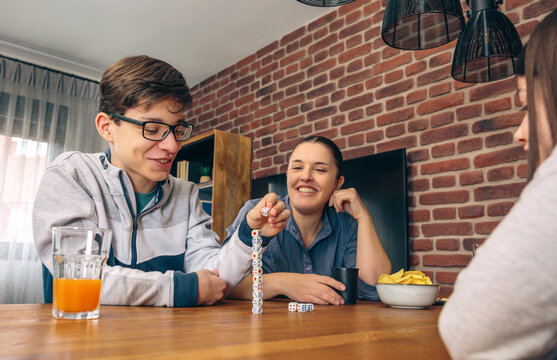 A son smiles as he adds a dice to a vertical stack while playing a game with his amused mother and sister during a family weekend