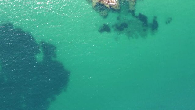 Toma cenital grabada con un dron. Movimiento de aproximaci&oacute;n al acantilado de la playa con olas. Mar verde claro y azulado, transparente. Vacaciones de verano, tranquilidad.