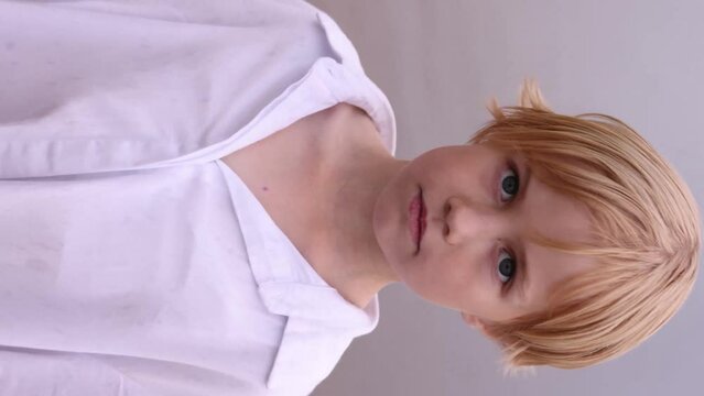 A beautiful blonde child turns her head and looks seriously at the camera. A dramatic image of a charming girl against the background of water.