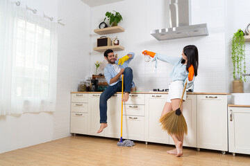 Girlfriend and boyfriend in rubber gloves singing and playing mop like guitar in kitchen. Happy...