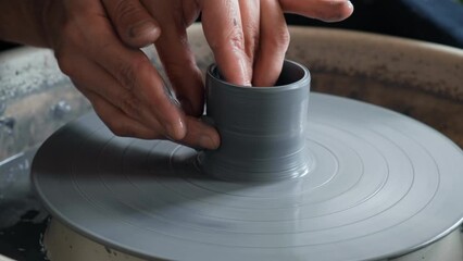Male hands making ceramic cup on pottery wheel. Man ceramicist working with gray clay in workshop creating a mug. Concept of creativity, handmade, hobby