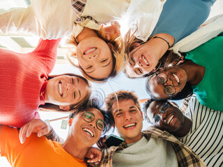 Low angle view of a group of multiracial friends standing on a circle, smiling and embracing...