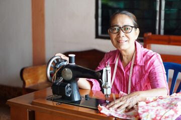 Happy senior Asian woman tailor is sewing cloth by vintage sewing machine at home. Concept, Senior...