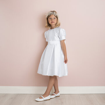 blonde girl 9 years old in a white festive dress on a pale pink background, dress for a wedding, first communion, birthday, celebration