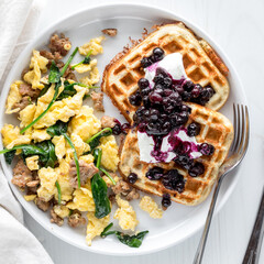Protein waffles topped with yogurt and sauteed berries along with scrambled eggs