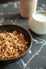 Close up view of whole grain cereal in a bowl with a cup of milk on a black marble kitchen table