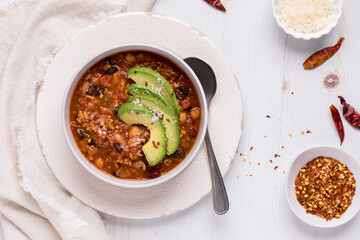A bowl of homemade black bean chili with fresh avocado slices and chili flakes.