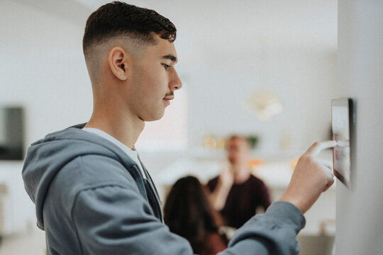 Side view of boy using home automation app through digital tablet mounted on wall