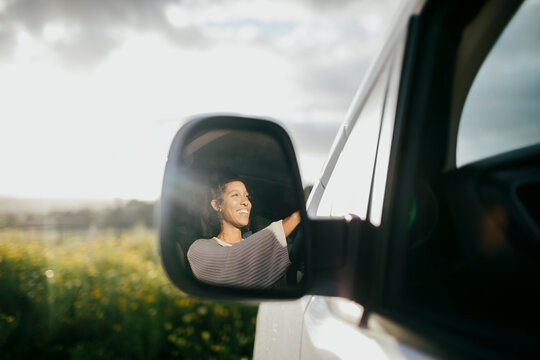 Happy young woman driving van seen through side-view mirror