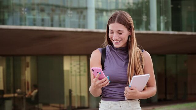 Slow motion of a happy teenager female smiling and typing on a smart phone using a social media app outdoors. Young woman having fun texting messages on a cellphone. Real lady using a mobilephone