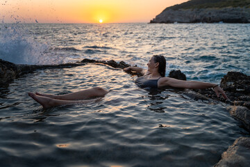 Young cheerful relaxed woman in a natural sea bath on the seashore. Thalassotherapy wellness concept - obrazy, fototapety, plakaty