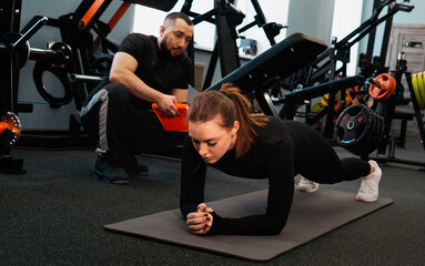 A female athlete performs a plank exercise. The coach encourages and monitors the correct posture.