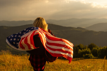 Young woman holding American flag on sky background