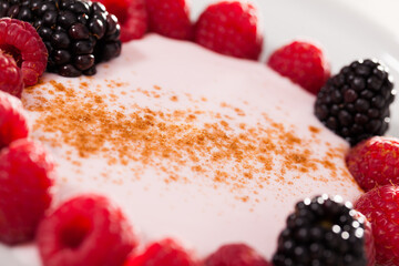 Raspberries and blackberries laid out on a white plate in circle with yogurt and cinnamon