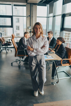 Portrait of smiling businesswoman with crossed hands standing in office on colleagues background