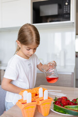 The process of making ice cream. Child making tasty ice lollipops in moulds on countertop in kitchen during free time.