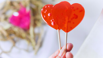 Valentine's Day concept. Female hand holding two red heart-shaped lollipops.