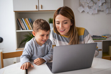 Happy mother and son using laptop at desk at home