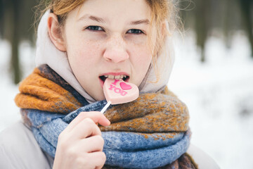 Cute teenager girl with freckles in the forest posing with Valentines day heart shaped lollipop....