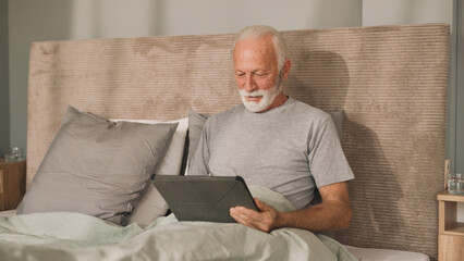 Senior man using digital tablet in bed