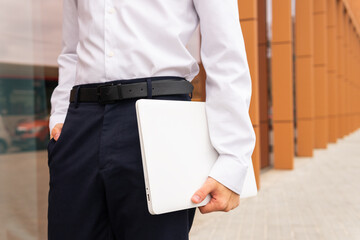Close-up of a professional anonymous man in a white shirt and navy pants holding a laptop, ready for a productive business day
