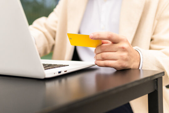 Close-up of anonimous businessman hand holding a credit card while using a laptop, indicating an online transaction or shopping