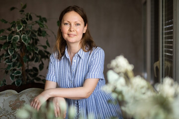 Portrait of charming dreaming woman at the window in her house
