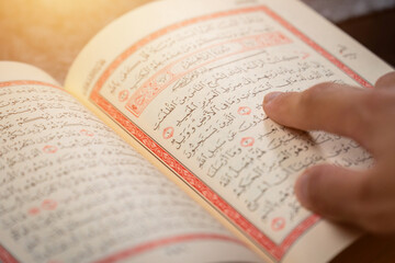 Quran (Koran) - close up of holy book of Muslims, with hand pointing ayat (Āyah), and shining...