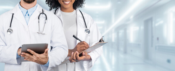 A male and female medical professional, one holding a tablet and the other with a clipboard