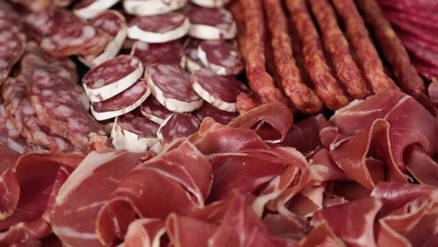 Meat plate with assortment of various tasty Spanish, french or Italian appetizers - sliced prosciutto, sausage, salami, kabanos sausages, fuet. Meat platter rotating